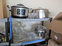 Photo showing Hamilton Beach crock pot, large roasting pan, chafing dish, and assorted glassware on a plastic shelf unit