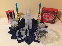 Overall view showing Mikasa bonbon dish, frosted nativity scene, silver plated candle holders with blue candles, frosted Santa figure and boxed crystal gift boxes on holiday fabric topper.