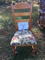 Front view of one wooden ladderback farmhouse chair with carved top and patterned upholstered seat with apple and leaf design outdoors.