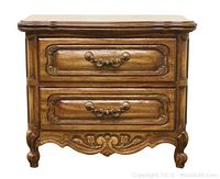 Front view of one of the matching brown wood night or end tables showing two drawers with ornate handles and carved details.
