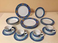 Full set of 20 piece stoneware service showing plates, bowls, cups, and saucers with colorful underwater-themed decorative rims in blue.