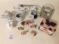 Overview of farm-themed ceramics, pig figurines, piggy bank, rolling pin, and decorative sign on white surface