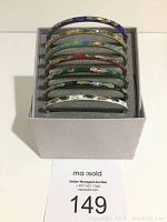 Front view of seven multi-colored cloisonne bracelets stacked inside a gray box, showing their color and pattern variety.