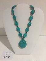 Full view of turquoise stone and sterling silver beaded necklace with large teardrop pendant on display bust.
