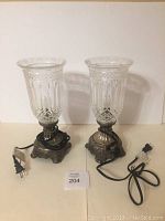 Photo of two glass table lamps with clear etched and cut hurricane-style shades and ornate metal bases. Lamps are unplugged.