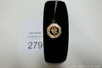 Front-view photo showing the 14K gold charm on a black stand; charm is octagonal with inscription and colored stones forming a flower in the center.