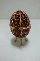 Front view of red enameled egg figurine with gold-tone detailing and rhinestones on three ornate legs.