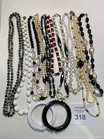 Overview of all necklaces and bracelets in lot, showing variety of bead styles in black, white, red, and clear beads, with two bangle bracelets at bottom