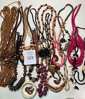 Photo showing an assortment of necklaces laid out, featuring various bead types, pendants, and cord materials in brown, black, pink, green, and red tones.