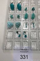 Full view of 7 pairs of turquoise fashion earrings arranged in clear plastic packaging including shells, stars, swirls, round beads, and bead dangles