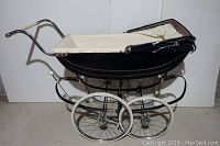 Side view of black vintage baby carriage with cream interior and chrome handles.