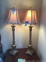 Pair of two bedside lamps with twisted metal bases and fabric shades, one lamp lit to show shade color and texture