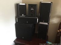 Photo of Yamaha surround sound system with five satellite speakers and one subwoofer arranged on a table showing front side and logos