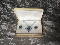 Vintage costume jewelry set including an 18-inch necklace with a blue stone pendant and matching clip-on earrings in a cream-colored box