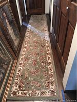 Photo of the full length of the wool hall runner rug placed in a hallway between wooden doors, showing its floral and vine pattern with a cream border.