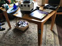 Full view of the wooden dining table with various items on top and the base of the table showing the legs and carpet underneath.