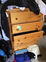 Front view of pine dresser with five drawers, some open, showing wooden drawer knobs and natural pine wood grain. Clothing and other items around dresser not included.