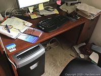 Photo showing the right side of the used wooden desk with keyboard, papers, and trash bin underneath.