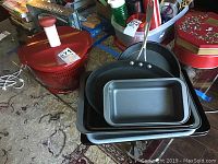 Photo showing Calphalon frying pan, bakeware stack, and red Kitchen Aid salad spinner on carpeted floor