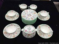 Top view of 4 cups on saucers, 2 extra cups and 14 side plates stacked in the center, surrounding sugar bowl with lid in the middle
