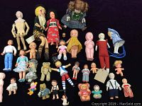 Photo showing a collection of vintage dolls and toys made from porcelain, bisque, celluloid, plastic, and plush material. Dolls vary in size and outfit style.