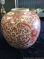 Front side view of round ceramic vase with intricate hand-painted red patterns on crackled glaze.
