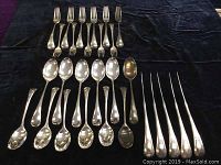 Photo showing full cutlery set laid out on dark cloth with dessert spoons, teaspoons, forks, knives, and salad forks.