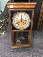 Full front view of the oak Sessions antique wall clock showing entire clock cabinet, dial, and glass lower door with inscription and medallion.