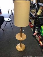 Full view of the vintage floor lamp showing the wooden base, integrated round table, and fabric shade at the top.