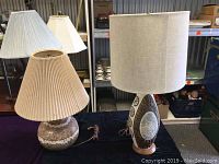 Three ceramic lamps displayed on a black tablecloth with a variety of shapes and shades visible