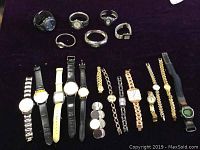 Overview of 20 assorted quartz watches laid out on dark fabric, various band styles and colors.