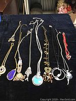 Lot of 10 vintage costume jewelry necklaces laid out on black fabric showing various pendant designs and chain types