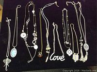Full view of all 10 necklaces laid on dark fabric showing style variety and pendant details.