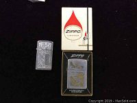 Lot overview showing two Zippo lighters, one in original box with instruction booklet, and the other lighter beside it with engraved design.