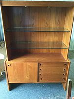 Front view of the vintage teak buffet showing top glass shelves and bottom drawers with sliding door.