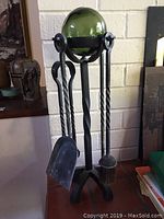 Photo showing full fireplace tool set on stand with green glass fishing net ball on top, including shovel, brush, poker and tongs.
