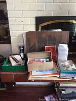Photo taken showing a wide view of the lot with boxes, books, and supplies arranged on a red brick hearth with a white brick background.