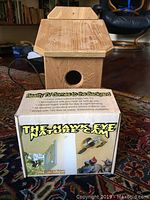 Wooden birdhouse sitting on top of The Hawk Eye Nature Cam box on carpet.