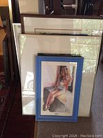 Photo showing overall view of several framed prints, focusing on a prominently displayed framed drawing of a woman in a blue frame.