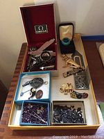 Photo of lots of assorted costume jewellery on a tray including shark teeth, pins, beads, cufflinks, and rings.