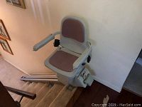 Stair lift seat mounted on dual rail at top of staircase