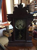Full frontal image of the wooden mantel clock showing overall carved details and clock face with Roman numerals.