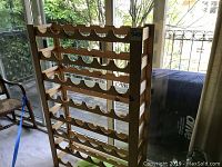 Front and side view of wooden wine rack with circular cutouts for holding wine bottles horizontally. Shows natural wood color and six levels.