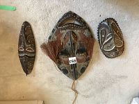 Photo showing all three African wood masks arranged flat on a light carpeted floor, highlighting relative sizes and overall condition.
