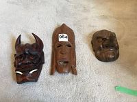 Three Pacific Island wood carved masks laid side by side on carpet showing sizes and different styles