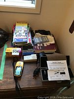 Various items on wooden table including Garmin eTrex GPS, refractometer, camera equipment, and manuals.