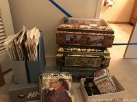 Three stacked decorative tins with magazines and a box of knitting supplies beside them