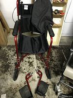 Full view of red lightweight transporter wheelchair with fabric seat and removed footrests lying in front.