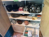 Photo of cabinet shelves displaying Corning Ware crockery, various glass and ceramic dishes, bowls, jars, and containers, including toast rack and ice cream dishes.