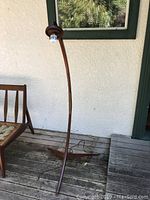 Full view of curved teak floor lamp standing next to a bench against a wall